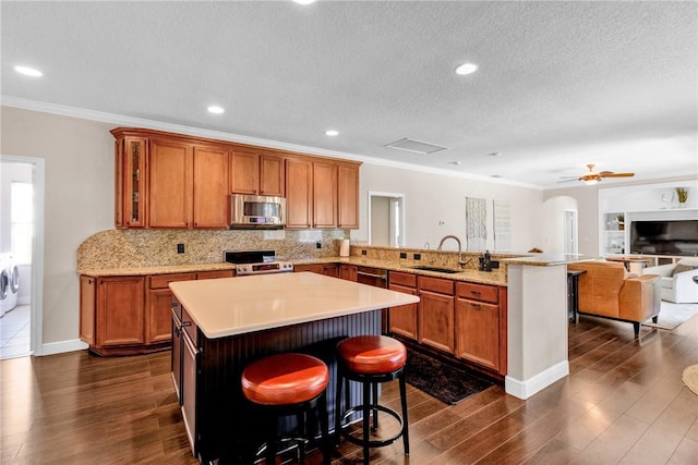 1337 Scarlet Oak Cir, Vero Beach, FL 32966 - kitchen featuring appliances with stainless steel finishes, brown cabinetry, ornamental molding, a peninsula, and a sink