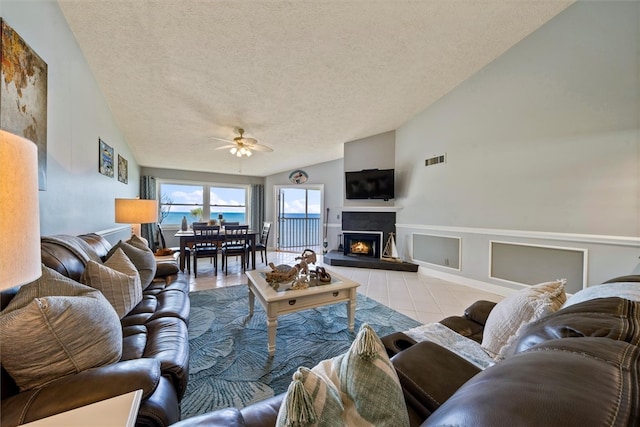 tiled living room featuring ceiling fan, a tiled fireplace, a textured ceiling, and vaulted ceiling