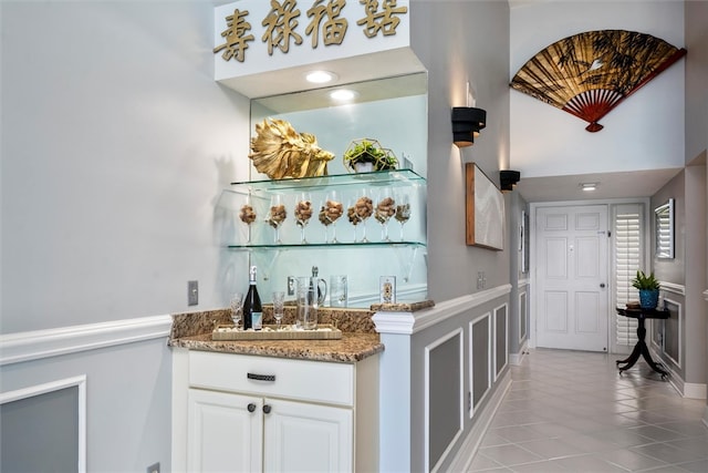 bar featuring stone countertops, white cabinetry, and light tile patterned floors