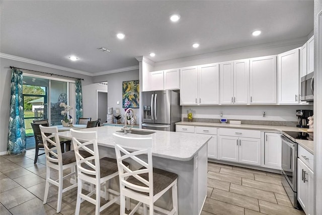 kitchen featuring a breakfast bar, appliances with stainless steel finishes, white cabinetry, a sink, and an island with sink