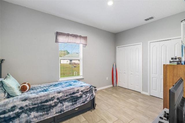 bedroom with light wood-type flooring, baseboards, visible vents, and multiple closets