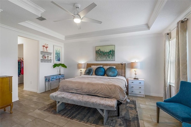 bedroom with a tray ceiling, a walk in closet, visible vents, and crown molding