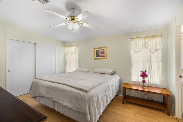 bedroom with light wood-style floors, ceiling fan, visible vents, and a closet