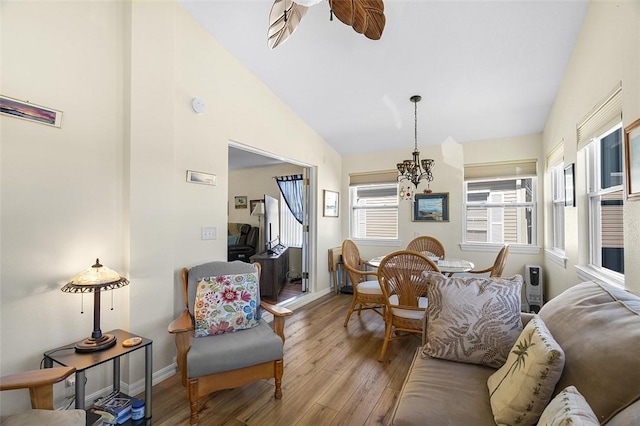 interior space featuring high vaulted ceiling, ceiling fan with notable chandelier, baseboards, and wood finished floors