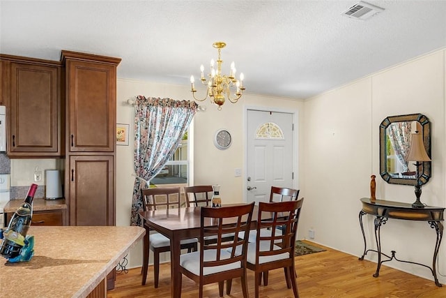 dining room featuring visible vents, ornamental molding, a textured ceiling, a chandelier, and light wood-type flooring