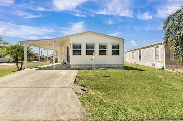 manufactured / mobile home featuring entry steps, concrete driveway, an attached carport, and a front lawn