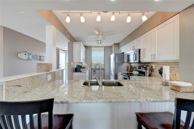 kitchen featuring a peninsula, a sink, appliances with stainless steel finishes, light stone countertops, and tasteful backsplash