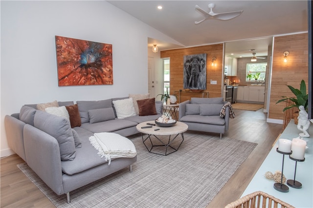 living room featuring light wood-type flooring, wood walls, ceiling fan, and sink