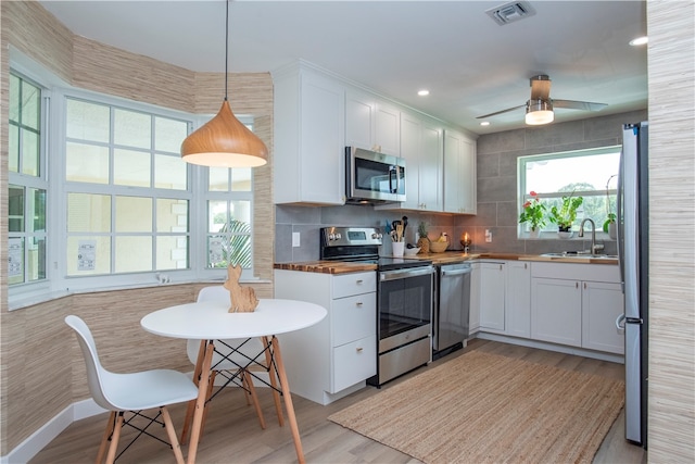 kitchen featuring appliances with stainless steel finishes, butcher block countertops, sink, white cabinets, and hanging light fixtures