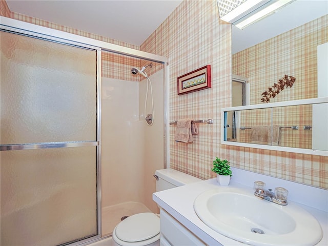 bathroom featuring a shower with door, vanity, and toilet