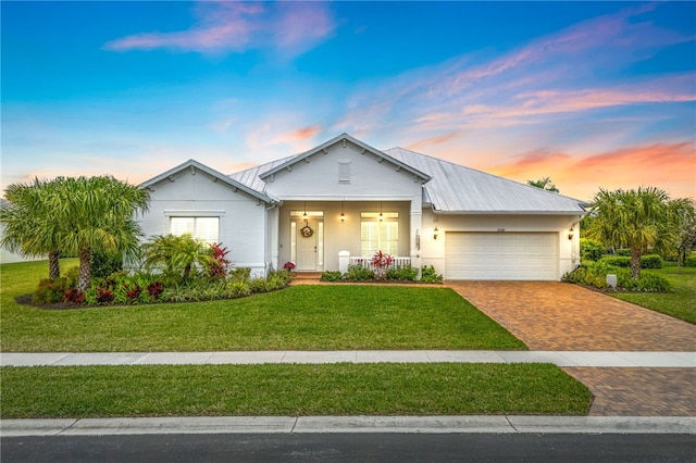 single story home featuring a garage, metal roof, covered porch, decorative driveway, and a front lawn