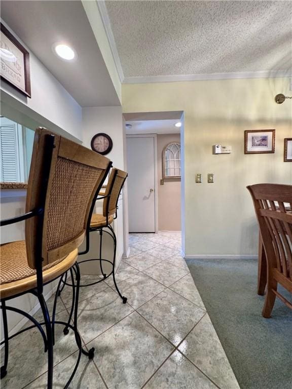 dining area featuring light carpet, a textured ceiling, baseboards, light tile patterned floors, and ornamental molding