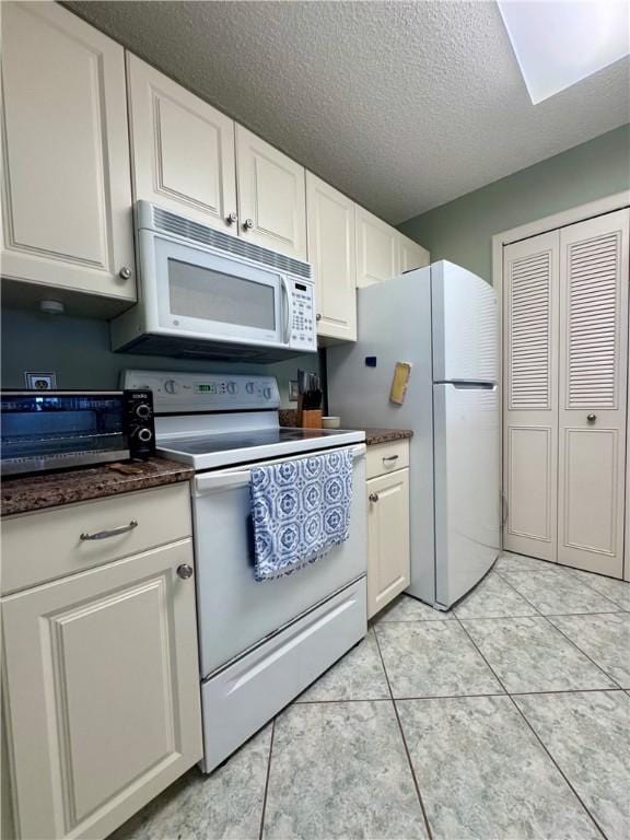 kitchen featuring dark countertops, a textured ceiling, white appliances, and white cabinetry