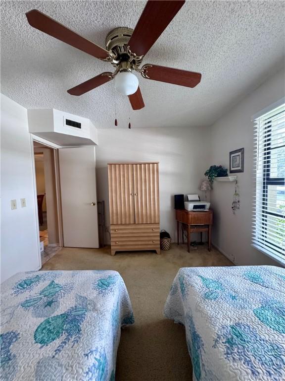 bedroom with a ceiling fan, carpet flooring, a textured ceiling, and visible vents
