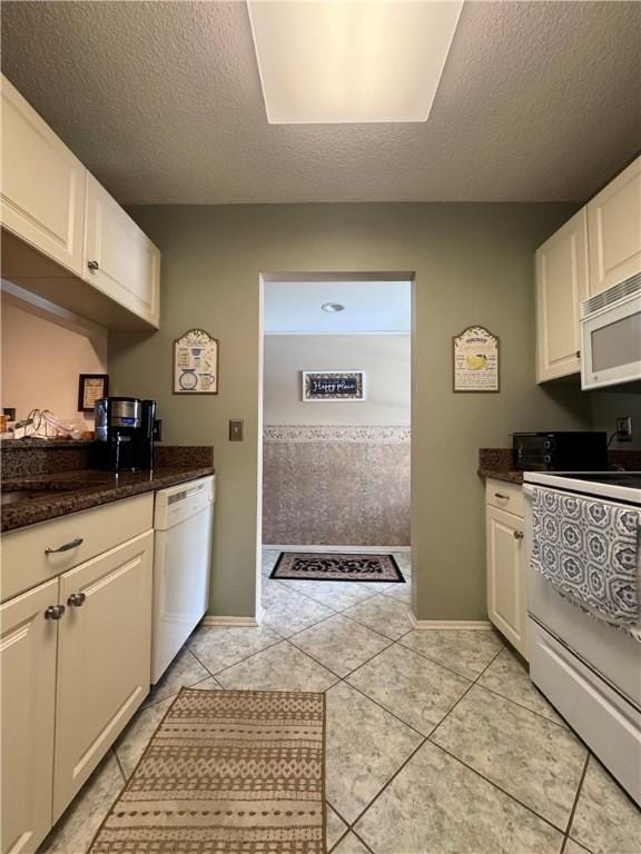 kitchen with light tile patterned floors, a textured ceiling, white appliances, and white cabinetry