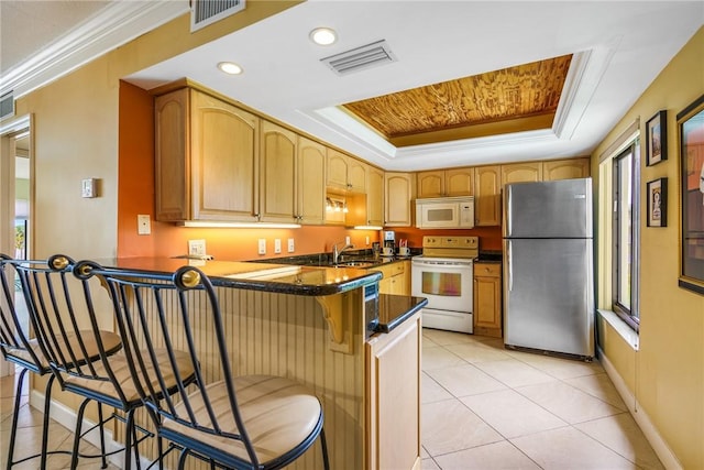 kitchen with kitchen peninsula, a kitchen breakfast bar, white appliances, a raised ceiling, and crown molding