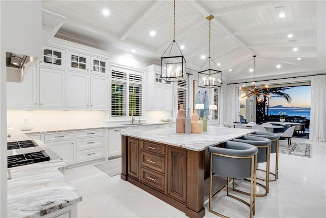 kitchen with sink, hanging light fixtures, vaulted ceiling with beams, a kitchen island, and white cabinetry