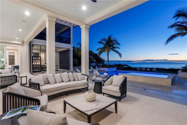 patio terrace at dusk featuring outdoor lounge area, a water view, and a balcony