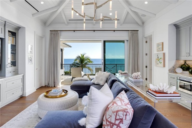 living room featuring beam ceiling, a water view, hardwood / wood-style flooring, and a notable chandelier