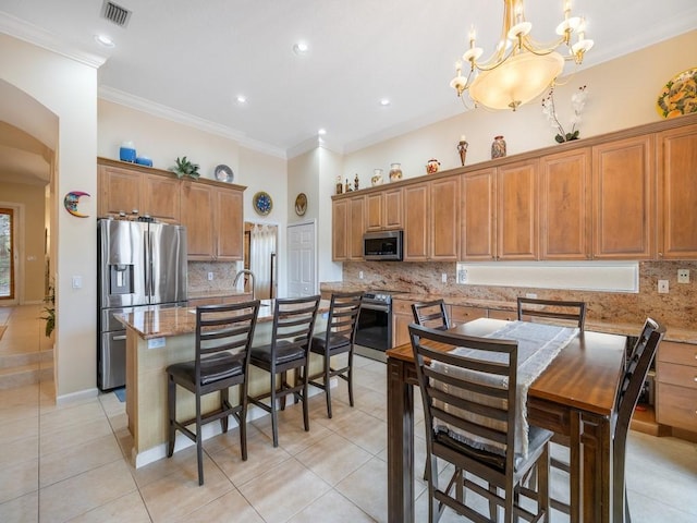 9535 E Maiden Ct, Vero Beach, FL 32963 - kitchen featuring stainless steel appliances, light tile patterned floors, decorative backsplash, brown cabinetry, and crown molding