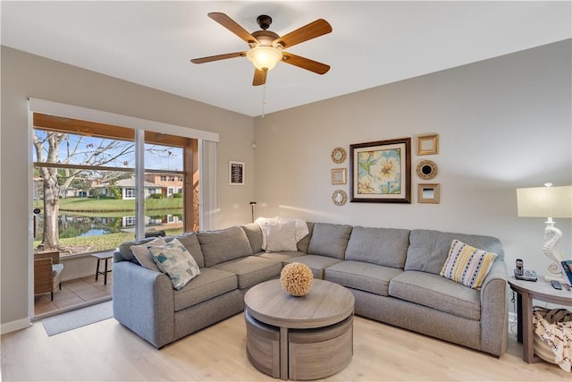 living room featuring light wood-type flooring, ceiling fan, and a water view