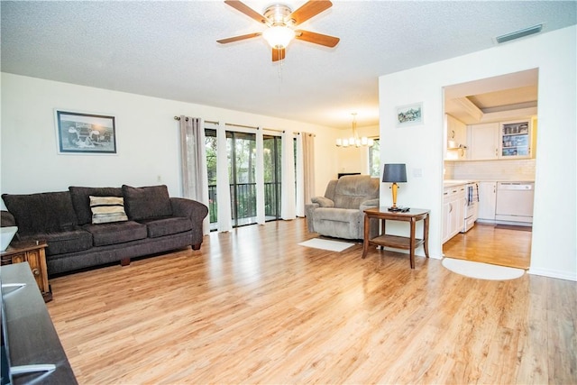 living room featuring a textured ceiling, a raised ceiling, ceiling fan with notable chandelier, and light hardwood / wood-style flooring