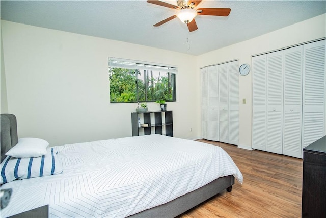 bedroom with ceiling fan, two closets, and light hardwood / wood-style floors