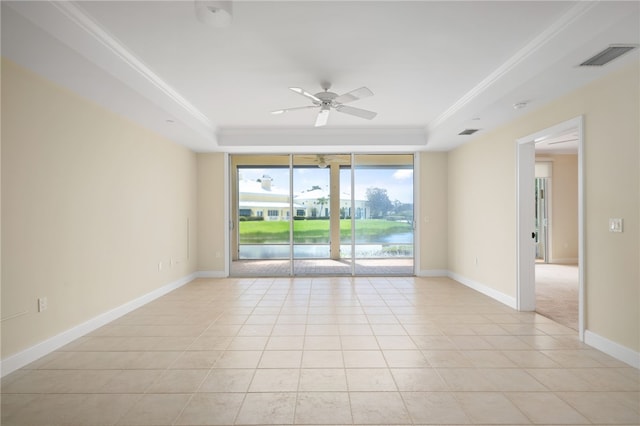 tiled empty room with ceiling fan, a raised ceiling, ornamental molding, and a water view