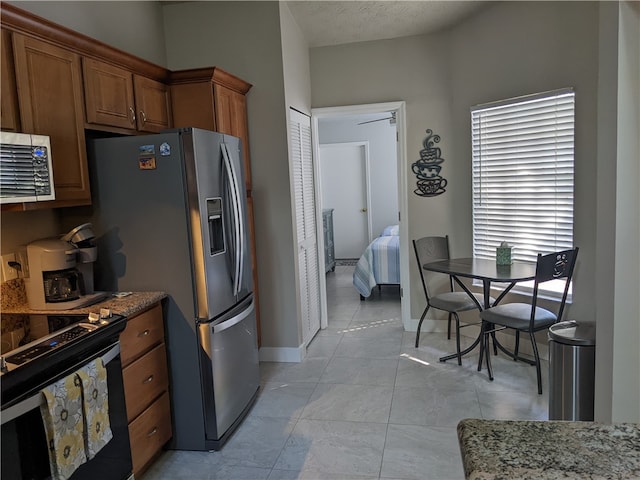 kitchen with stainless steel fridge, a textured ceiling, black range with electric stovetop, and light stone counters