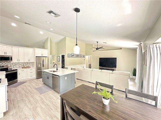 kitchen with a center island with sink, stainless steel appliances, decorative light fixtures, sink, and white cabinets