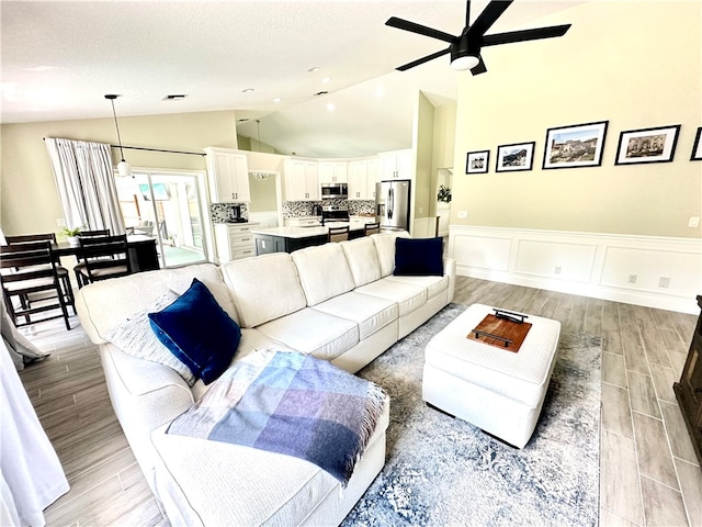 living room featuring a textured ceiling, light wood-type flooring, lofted ceiling, and ceiling fan