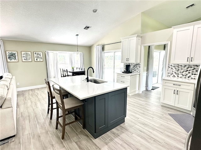 kitchen featuring light hardwood / wood-style floors, sink, lofted ceiling, white cabinets, and pendant lighting