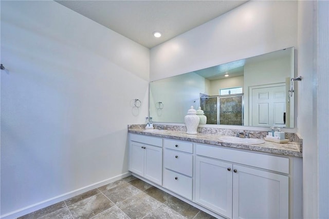 full bathroom featuring double vanity, a shower stall, baseboards, and a sink