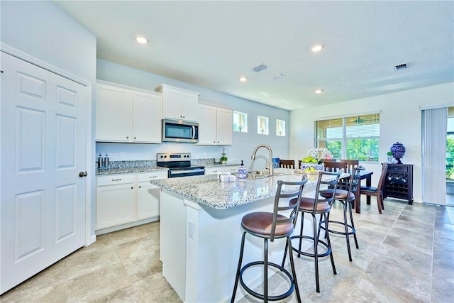 kitchen with light stone counters, stainless steel appliances, a kitchen bar, and visible vents