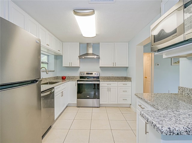 kitchen featuring stainless steel appliances, light stone counters, light tile patterned floors, white cabinets, and wall chimney range hood