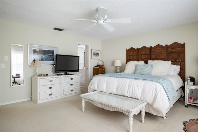 bedroom with ceiling fan, ensuite bath, light carpet, and a textured ceiling