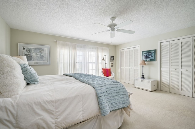 carpeted bedroom with ceiling fan, a textured ceiling, and multiple closets