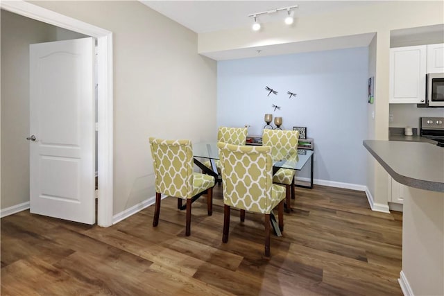 dining space featuring dark wood-type flooring, baseboards, and rail lighting