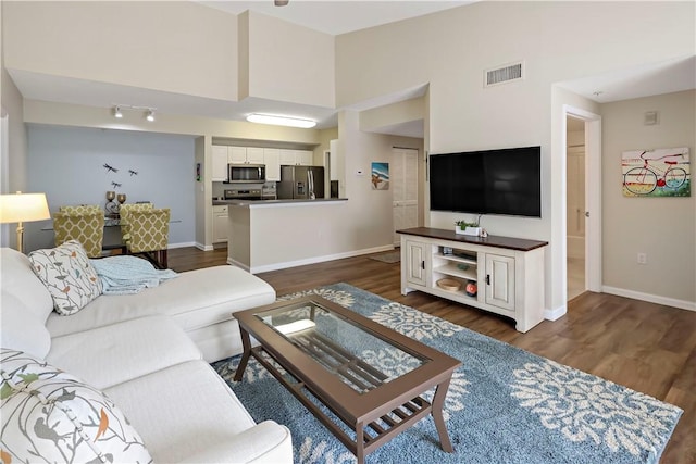 living area with baseboards, dark wood finished floors, and a towering ceiling
