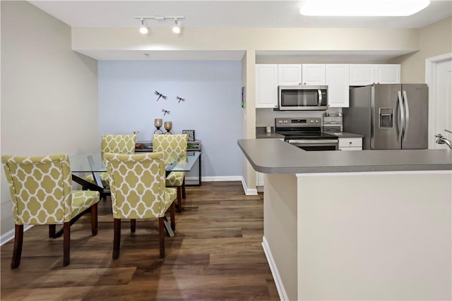 kitchen featuring appliances with stainless steel finishes, white cabinetry, dark wood-style flooring, rail lighting, and baseboards