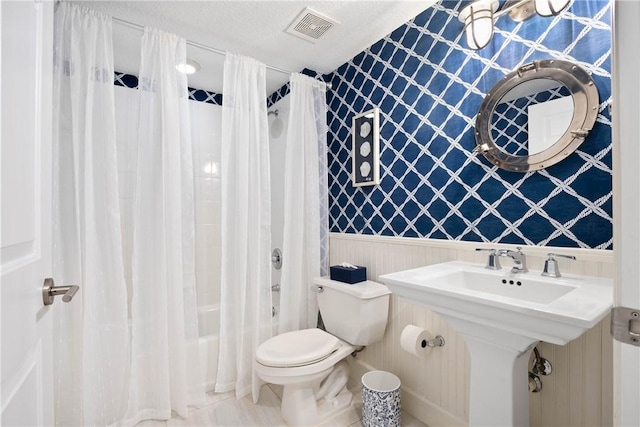 full bathroom featuring toilet, shower / bath combination with curtain, sink, and a textured ceiling