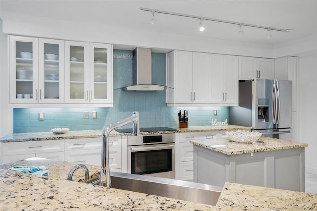 kitchen featuring decorative backsplash, white cabinetry, stainless steel appliances, and wall chimney range hood