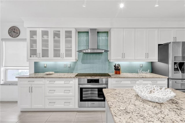 kitchen featuring appliances with stainless steel finishes, backsplash, wall chimney range hood, white cabinets, and light stone counters