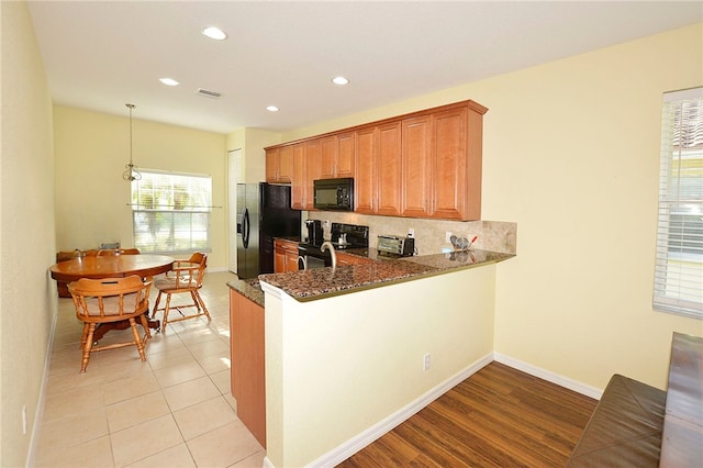 kitchen with kitchen peninsula, plenty of natural light, dark stone counters, and black appliances