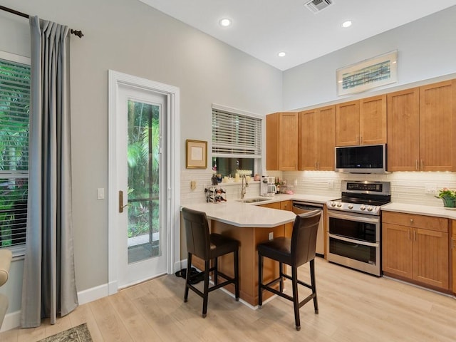 kitchen with a kitchen bar, sink, light hardwood / wood-style flooring, appliances with stainless steel finishes, and kitchen peninsula