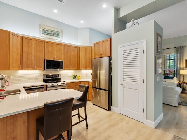 kitchen with sink, stainless steel appliances, a kitchen breakfast bar, kitchen peninsula, and light wood-type flooring