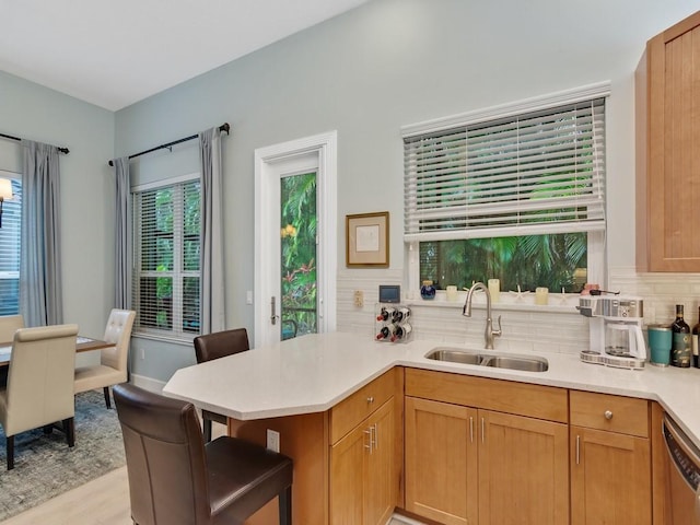 kitchen with sink, a kitchen breakfast bar, kitchen peninsula, dishwasher, and light hardwood / wood-style floors