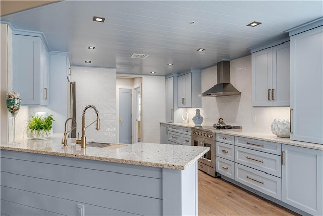 kitchen with wall chimney range hood, sink, light hardwood / wood-style flooring, light stone counters, and kitchen peninsula