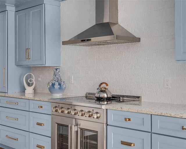 kitchen with high end stainless steel range oven, light stone countertops, wall chimney range hood, and decorative backsplash