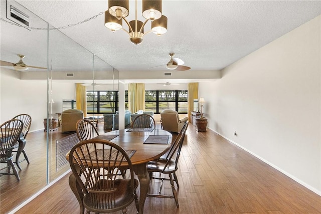 dining space with visible vents, wood finished floors, baseboards, a textured ceiling, and ceiling fan with notable chandelier